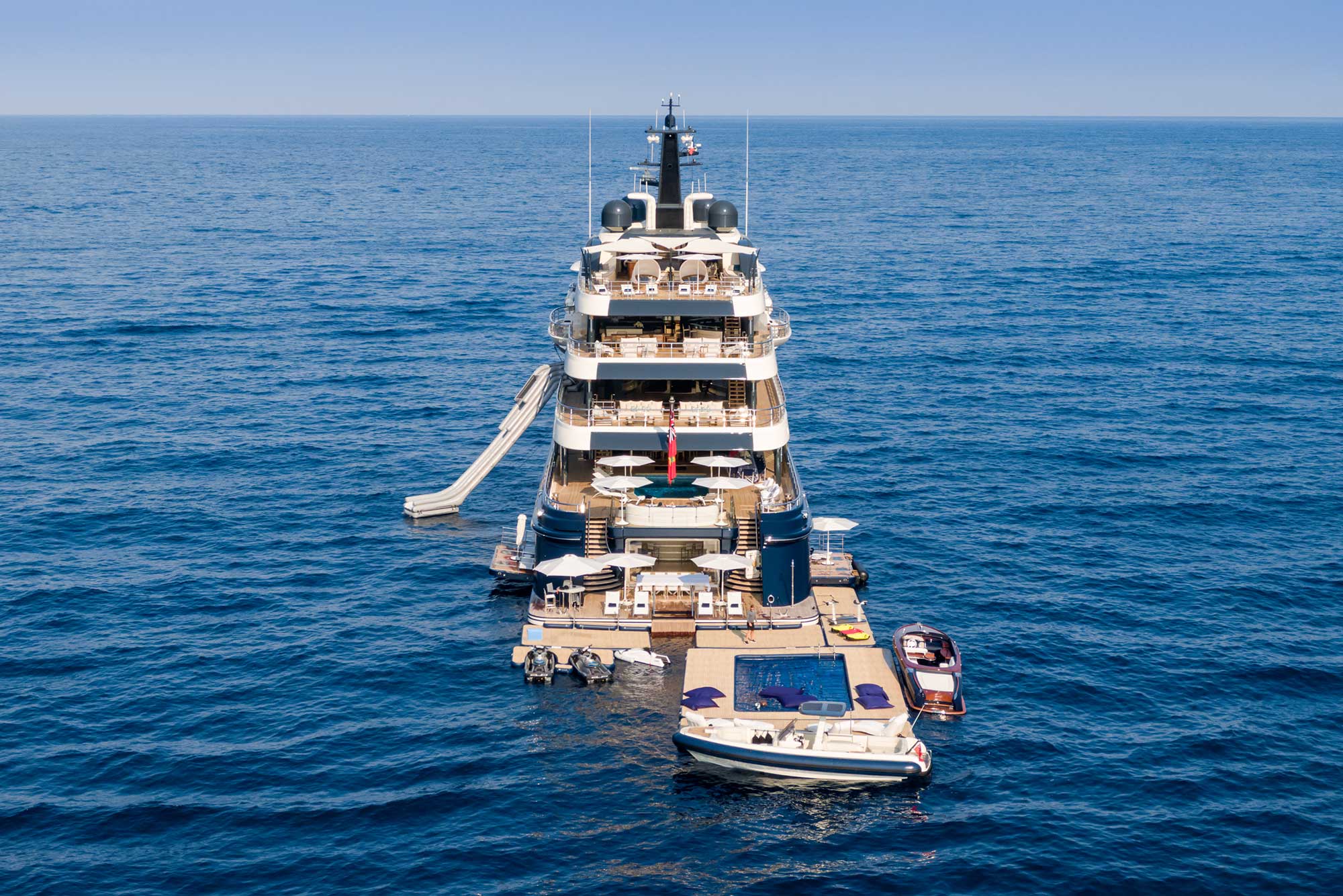 A large superyacht floating in the middle of the ocean, surrounded by luxurious tenders and toys.