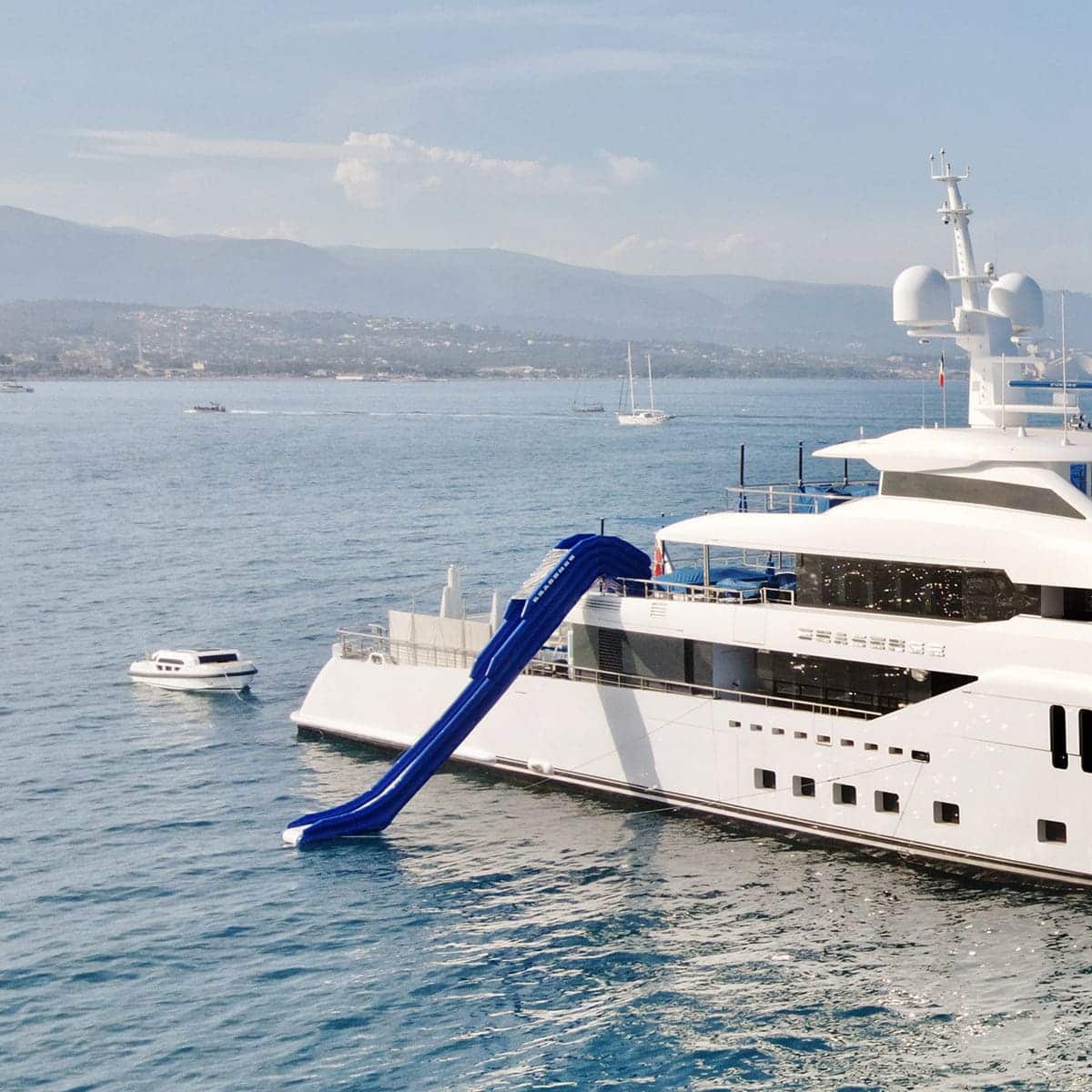 A large white yacht with a bright blue inflatable slide.